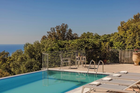 A swimming pool with lounge chairs and a view of the sea.