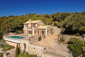 Una villa de piedra con piscina, una escalera de piedra y vistas del bosque circundante.
