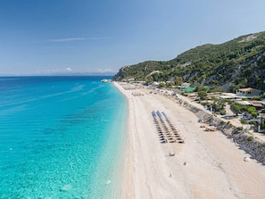 A beach with clear turquoise water, a long stretch of sandy shore, and a row of beach umbrellas.
