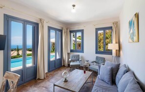 A room with a pool view, large windows, a sofa, a table, and a lamp.