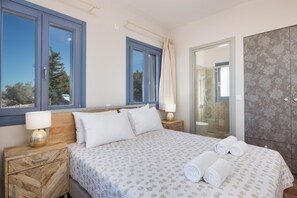 A bedroom with a bed, two bedside tables, a nightstand, a window, and a door leading to a bathroom.
