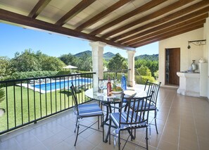 Un patio cubierto con vista a la piscina, mobiliario exterior y una chimenea de piedra.