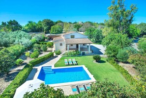 Una villa con piscina, rodeada de exuberante vegetación y un cielo azul brillante.