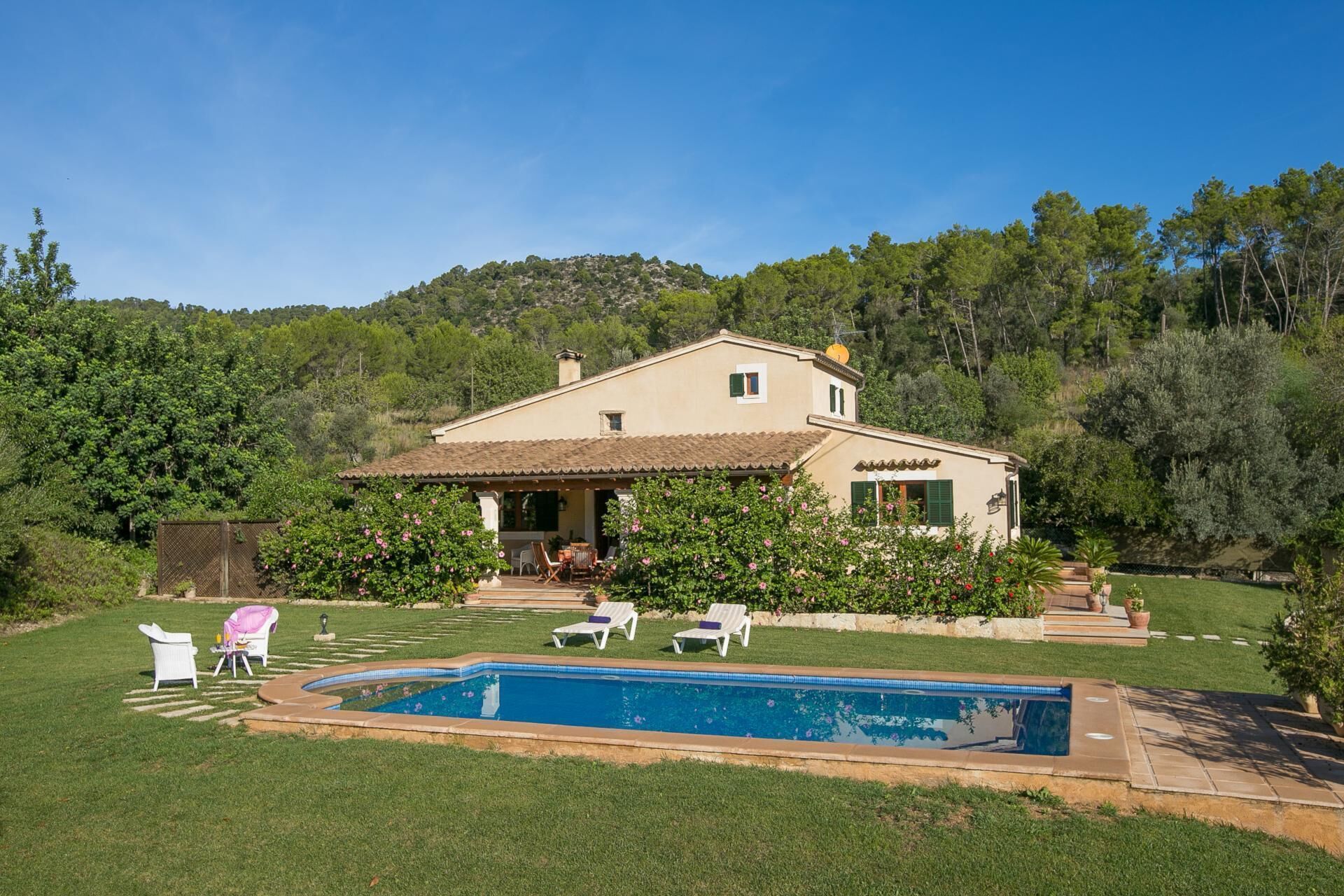 Ein zweistöckiges Haus mit Swimmingpool, umgeben von viel Grün und Hügeln.