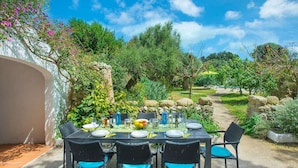 An outdoor dining area with a table set for four, surrounded by greenery and a stone wall. - Talati de Dalt - Five Bedroom Villa, Sleeps 8 (Alaior)