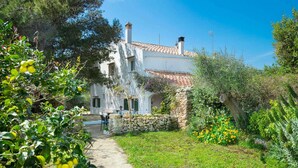 A white building with a tiled roof, stone walls, and a stone pathway leading to a table and chairs. - Talati de Dalt - Five Bedroom Villa, Sleeps 8 (Alaior)