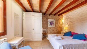 Een slaapkamer met een bed, nachtkastjes, een stoel, een kledingkast en een stenen muur.