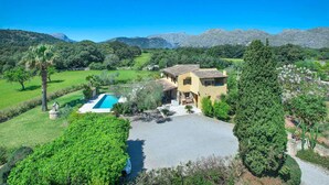 Een villa in mediterrane stijl met een zwembad, omgeven door weelderige begroeiing en bergen.