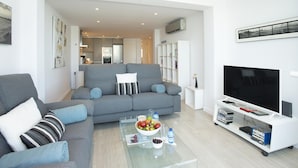 A modern living room with a grey sofa, a glass coffee table with fruits and drinks, a flat-screen TV, and a bookshelf. - Pine Walk Apartment - Three Bedroom Villa, Sleeps 5 (Mallorca)