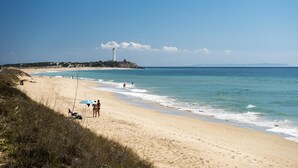 A beach with a lighthouse in the distance, clear skies, and calm waters.