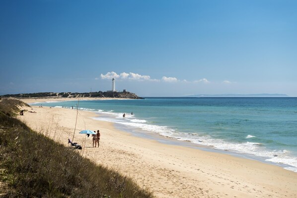 A beach with a lighthouse in the distance, clear skies, and calm waters.