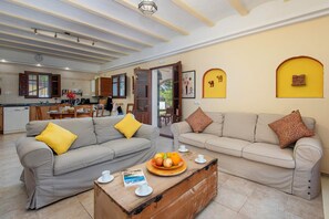 A living room with two sofas, a coffee table with fruit, and a kitchen in the background. - Casa de la Fuente - Two Bedroom Villa, Sleeps 4 (Vejer de la Frontera)