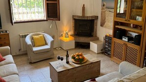 A cozy living room with a fireplace, a sofa, a coffee table with drinks, and a wooden cabinet with glassware.