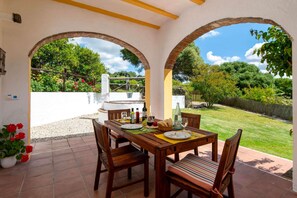An outdoor patio with a wooden table set for dining, surrounded by arches, and a view of a garden. - Casa de la Fuente - Two Bedroom Villa, Sleeps 4 (Vejer de la Frontera)
