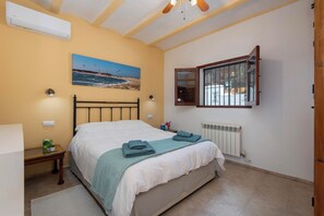 A bedroom with a bed, a painting of a beach, a window with bars, and a radiator. - Casa de la Fuente - Two Bedroom Villa, Sleeps 4 (Vejer de la Frontera)