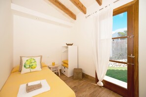 A bedroom with a bed, a bedside table, a small stool, and a window with curtains.