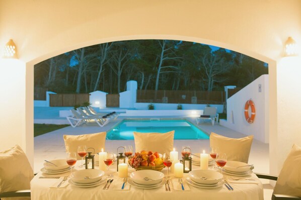 A dining table set for a meal with a view of a swimming pool and outdoor seating.