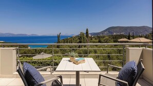 Um terraço com mesa e cadeiras, com vista para a costa e montanhas ao longe.
