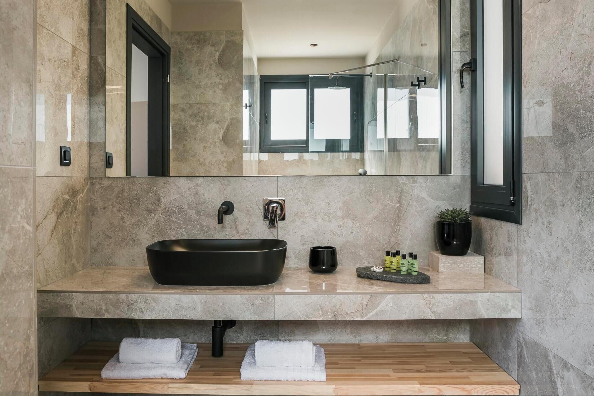 Une salle de bain moderne avec un grand lavabo noir sur pied, une petite tasse noire et une plante en pot posée sur le meuble-lavabo.