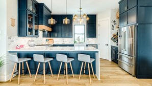 Una cucina moderna con mobili scuri, un'isola grande con sgabelli da bar, elettrodomestici in acciaio inossidabile e luci a sospensione.
