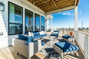 A covered outdoor deck with wicker furniture, large windows, and a view of the ocean.