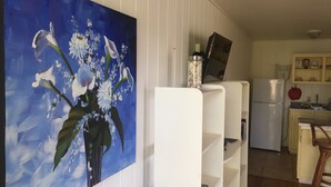 Ein Wohnzimmer mit einem großen Blumenbild, einem weißen Regal und einer Küchenzeile mit Kühlschrank und Schränken.