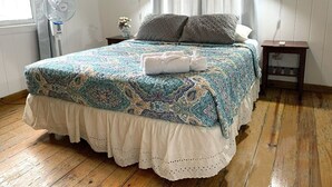 Ein Schlafzimmer mit einem Bett, einem Nachttisch, einem Wandventilator und einem Fenster mit Vorhängen.