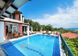 Una piscina con sillas de descanso y zona de comedor, rodeada de vegetación y un cielo despejado.