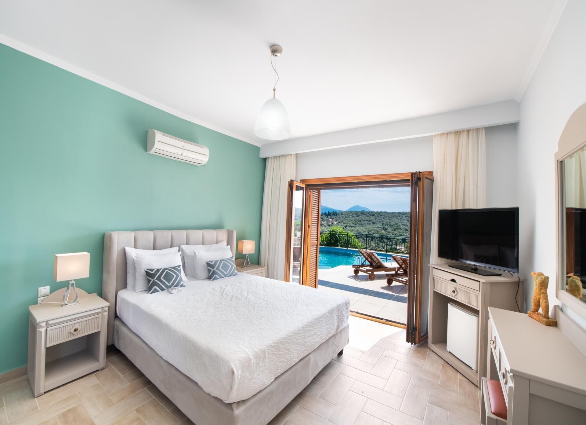 Un dormitorio con cama, televisor, escritorio y vista a una piscina y montañas.