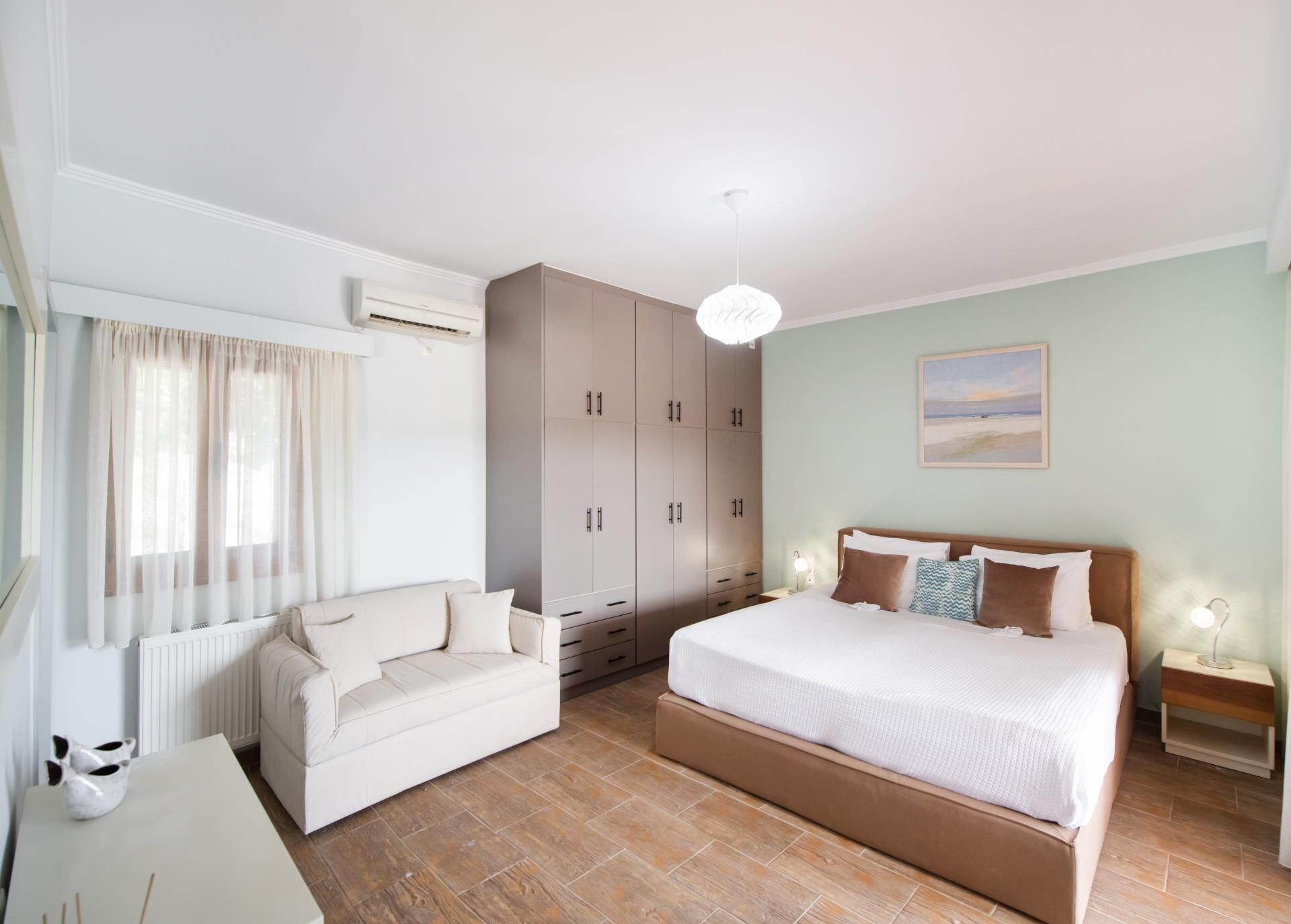A bedroom with a bed, a sofa, a wardrobe, and a painting on the wall.