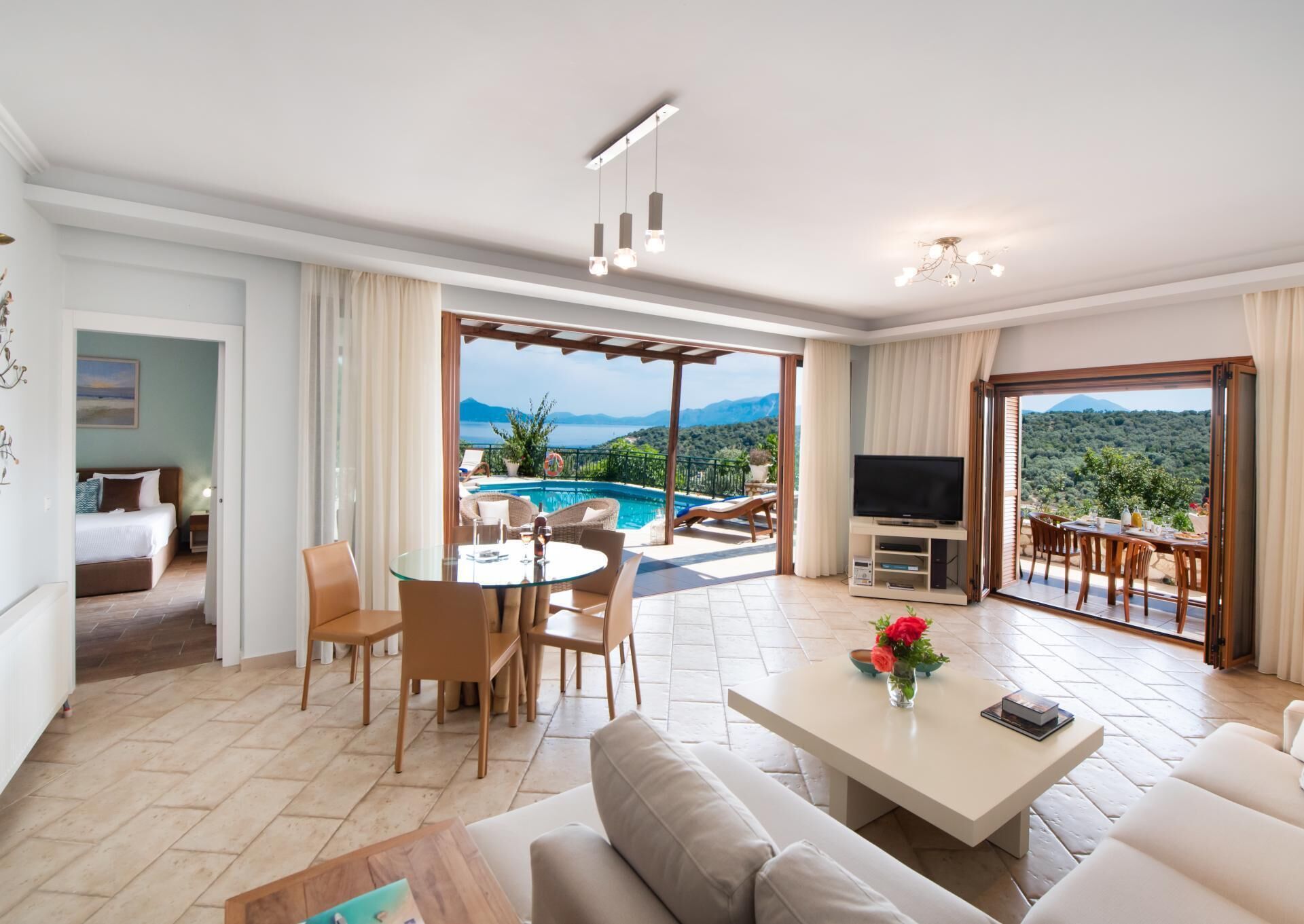 Ein modernes Wohnzimmer mit Blick auf einen Pool, einem Fernseher und einem Essbereich mit Gartenmöbeln.