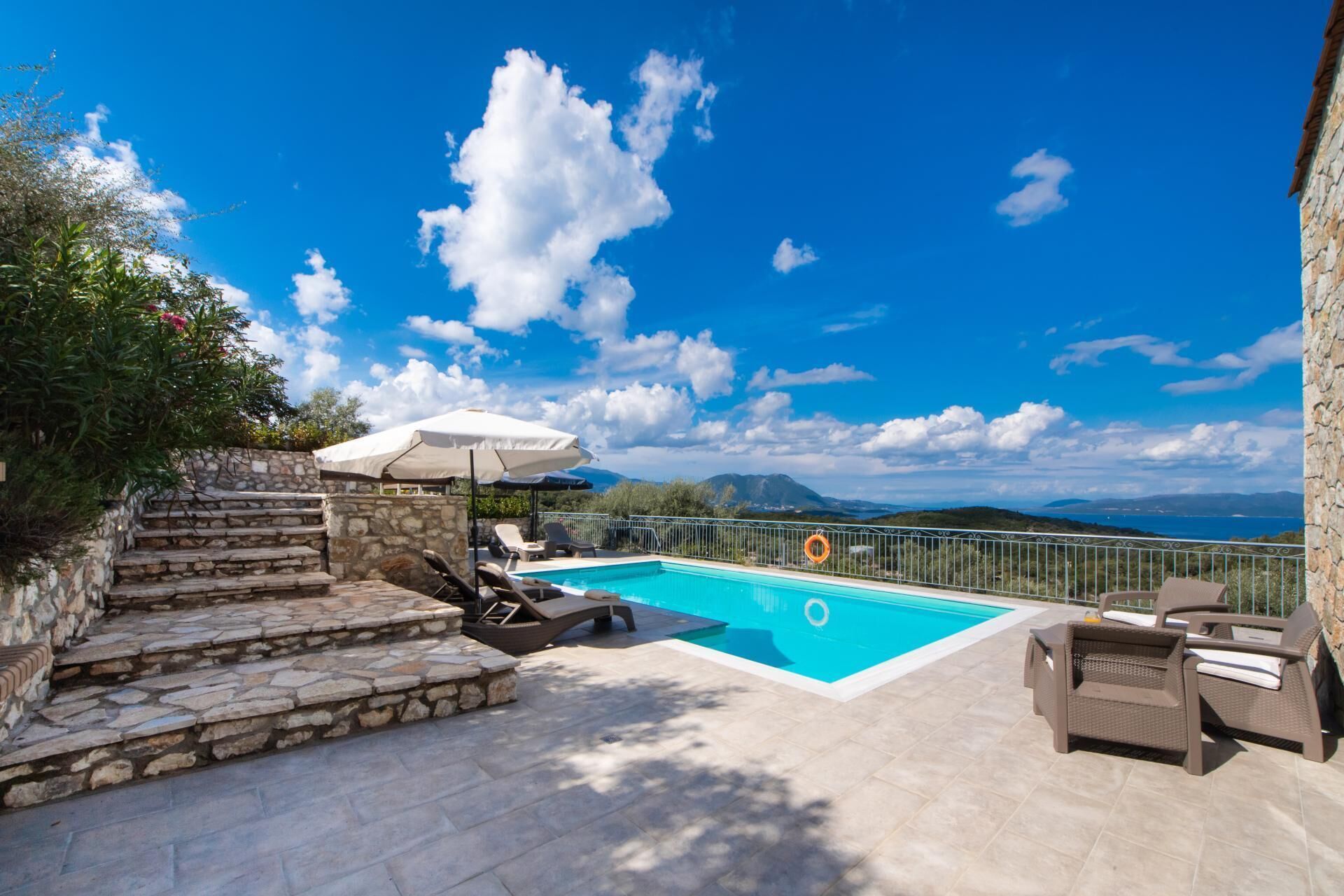 A pool area with stone steps, lounge chairs, and a view of the sea and mountains.
