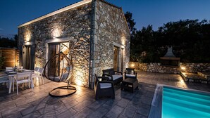 Un edificio de piedra con piscina, mobiliario exterior y una silla colgante.
