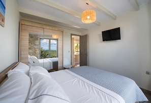 A bedroom with a large bed, a television mounted on the wall, and a view of the outdoors through a door.