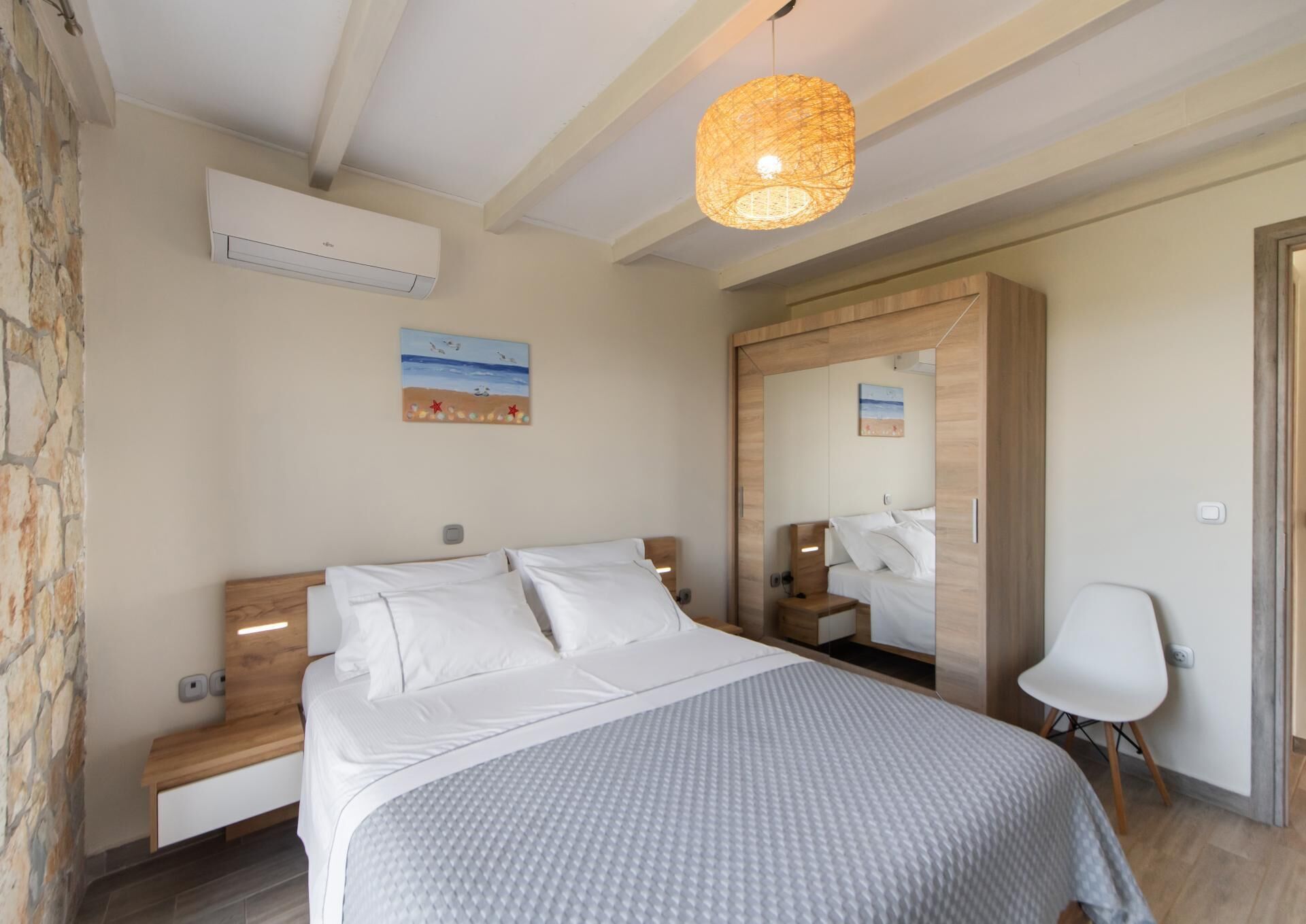 Un dormitorio con cama, mesitas de noche, un espejo, una silla y una lámpara colgante.