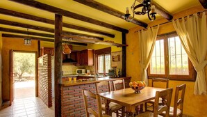 Een rustieke keuken met een bakstenen muur, houten balken en een eettafel met stoelen.