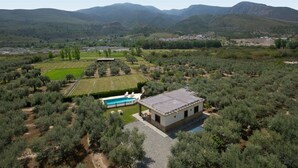 Een villa met zwembad, omgeven door olijfbomen en velden, met een bergachtig landschap op de achtergrond.