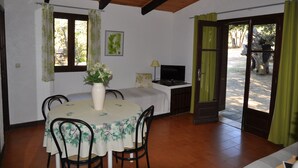 Zona pranzo con tavolo apparecchiato per quattro persone, un vaso con fiori, un televisore su un mobile e una porta che dà sull'esterno.