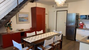A dining area with a table set for four, a red cabinet, a painting, and a staircase. - Elegant apartment in the seaside park in Marina Centro (Rimini)