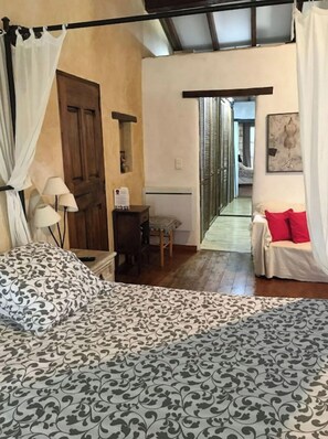 Ein Schlafzimmer mit einem Bett, einem Schreibtisch, einem Stuhl und einem Schlafsofa. Eine Tür und ein Fenster mit Jalousien sind ebenfalls vorhanden.