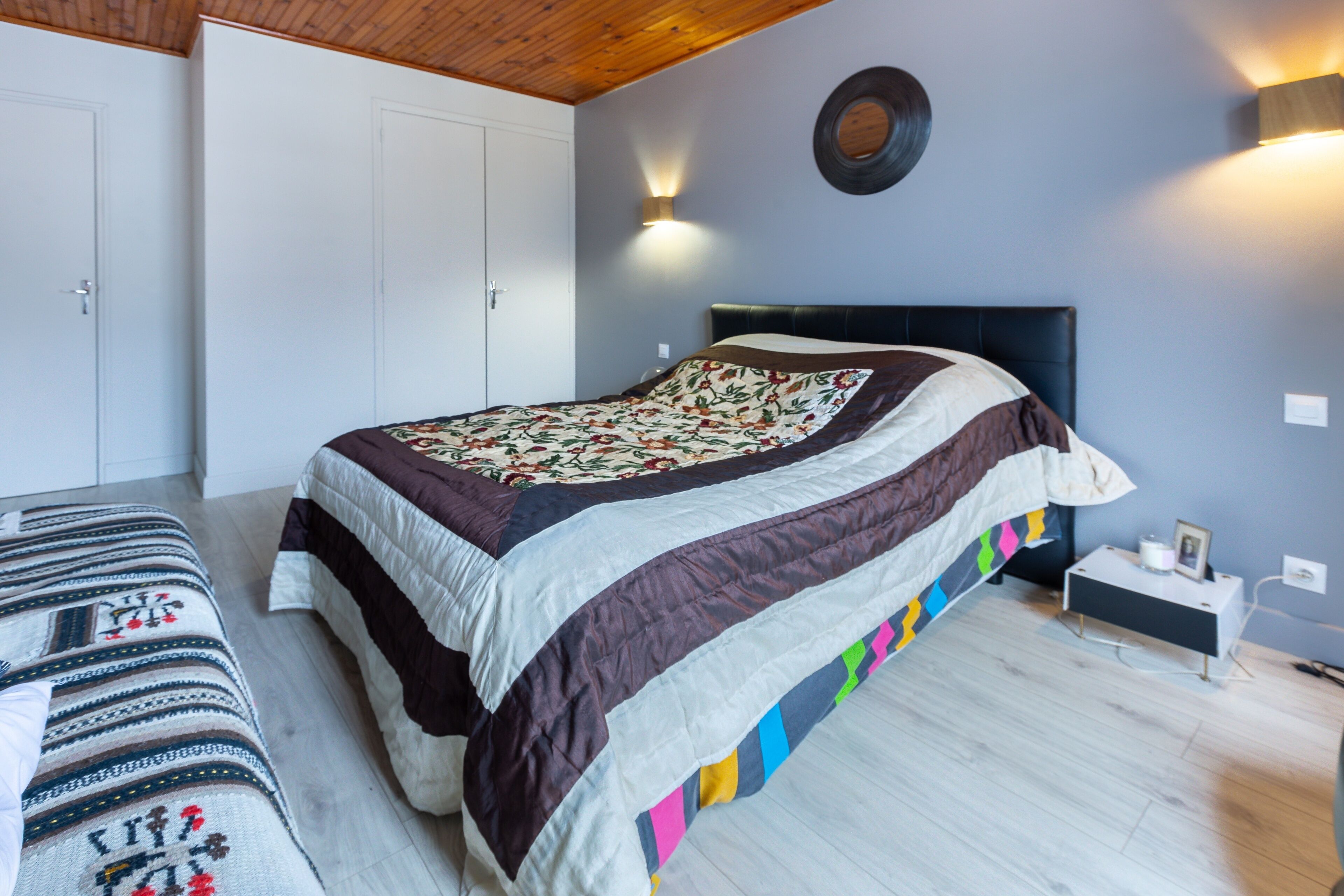 Een slaapkamer met een bed, nachtkastje, lamp, wandklok en een kledingkast.