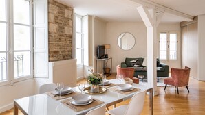 Un comedor con una mesa larga dispuesta para seis comensales, una pared de piedra y un sofá verde al fondo.