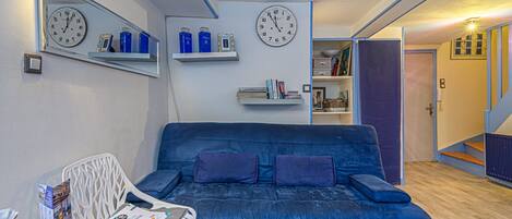 A living room with a blue sofa, two clocks on the wall, and a staircase leading to another room.