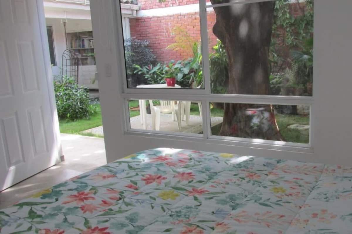 A room with a bed, a window, and a view of a garden.