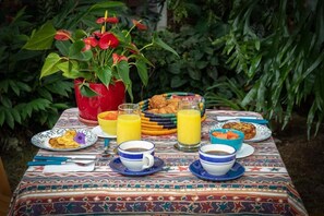 A breakfast table with plates of food, glasses of orange juice, and a red flower vase. - 50N15 B&B (Cali)