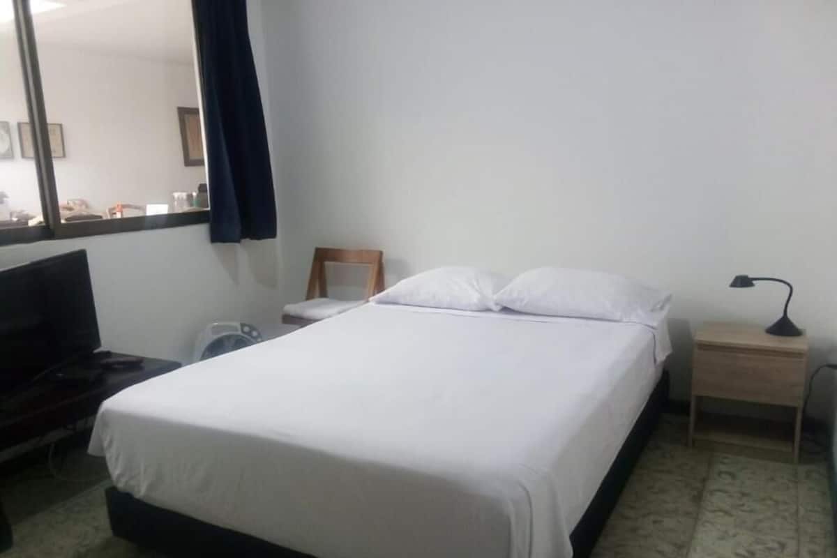 A hotel room with a bed, a desk, a chair, a TV, and a lamp.