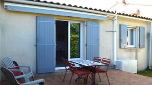 Um pátio com mesa e cadeiras, uma porta de correr e uma janela com persianas.