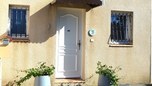 Um edifício com porta branca, duas janelas com grades de metal e plantas em vasos à frente.