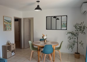 Een eetgedeelte met een ronde tafel, vier stoelen, een hanglamp, een spiegel aan de muur en een potplant.