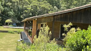 Un edificio rústico con fachada de ladrillo y techo metálico, rodeado de abundante vegetación y árboles.